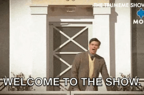 A Man In A Suit Is Standing In Front Of A Building With The Words Welcome To The Show Written On It . GIF