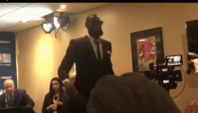 A Man In A Suit Is Standing In Front Of A Camera In A Room GIF