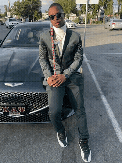 A Man In A Suit Is Standing In Front Of A Car That Says Kappa Alpha GIF