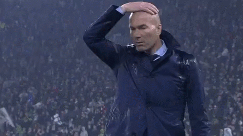 A Man In A Suit Is Standing In Front Of A Crowd And Covering His Nose With His Hand . GIF