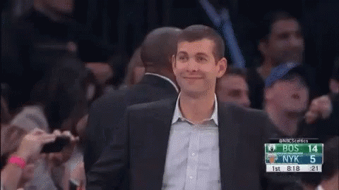 A Man In A Suit Is Standing In Front Of A Crowd Watching A Basketball Game Between Bos And Nyk . GIF