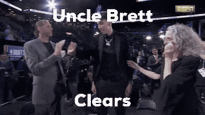 A Man In A Suit Is Standing In Front Of A Crowd With The Words Uncle Brett Clears Written Above Him . GIF