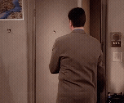 A Man In A Suit Is Standing In Front Of A Door With His Arms Crossed . GIF
