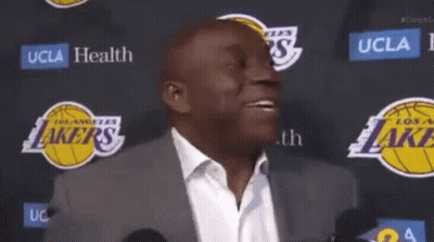 A Man In A Suit Is Standing In Front Of A Lakers Logo GIF