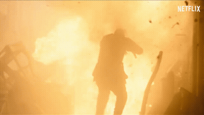 A Man In A Suit Is Standing In Front Of A Large Explosion With Netflix Written On The Bottom GIF
