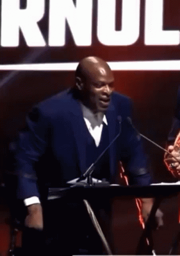 A Man In A Suit Is Standing In Front Of A Microphone And Talking Into It . GIF
