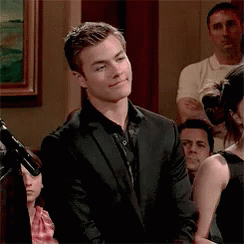 A Man In A Suit Is Standing In Front Of A Microphone In A Crowd . GIF