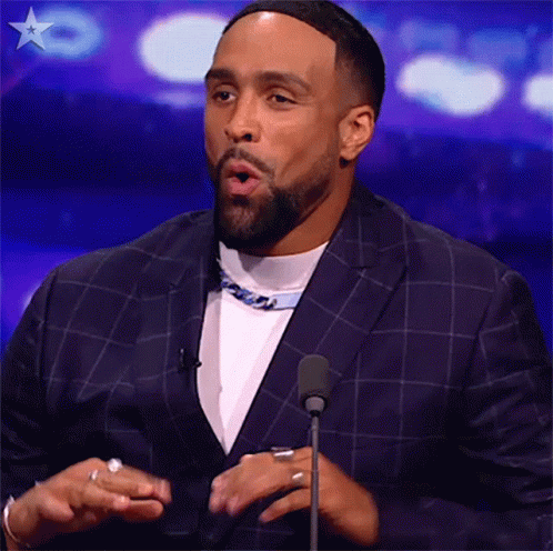 A Man In A Suit Is Standing In Front Of A Microphone . GIF