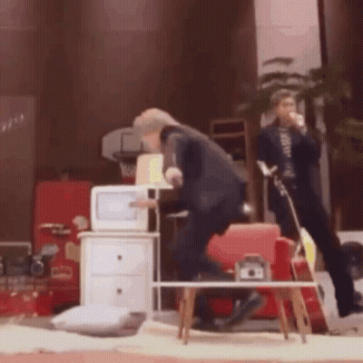 A Man In A Suit Is Standing In Front Of A Microwave In A Living Room GIF