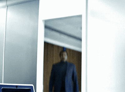 A Man In A Suit Is Standing In Front Of A Mirror In A Room GIF