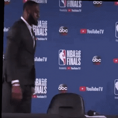 A Man In A Suit Is Standing In Front Of A Nba Finals Backdrop . GIF