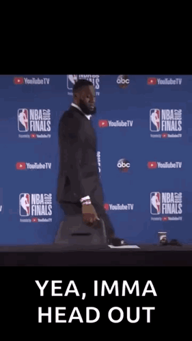A Man In A Suit Is Standing In Front Of A Nba Finals Sign GIF