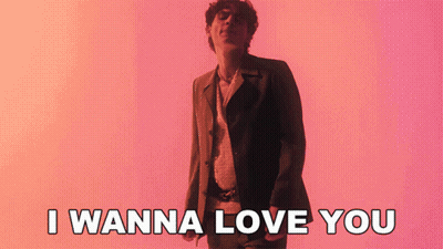 A Man In A Suit Is Standing In Front Of A Pink Background And Says I Wanna Love You GIF