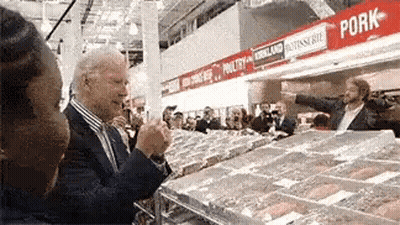 A Man In A Suit Is Standing In Front Of A Pork Section Of A Grocery Store GIF