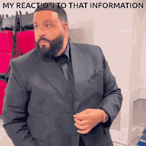A Man In A Suit Is Standing In Front Of A Row Of Red Seats With The Words " My Reaction To That Information " Underneath GIF