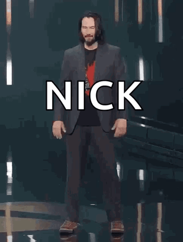 A Man In A Suit Is Standing In Front Of A Sign That Says Nick You 'Re Breathtaking ! GIF