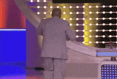 A Man In A Suit Is Standing In Front Of A Stage With Lights Behind Him GIF