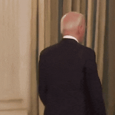A Man In A Suit Is Standing In Front Of A Wall GIF