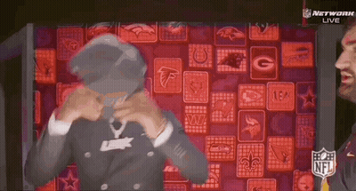 A Man In A Suit Is Standing In Front Of A Wall Of Nfl Logos . GIF
