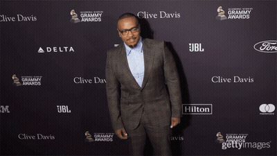A Man In A Suit Is Standing In Front Of A Wall That Says Clive Davis On It GIF