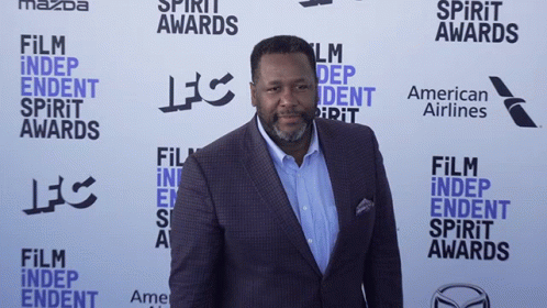 A Man In A Suit Is Standing In Front Of A Wall That Says Film Independent Spirit Awards GIF
