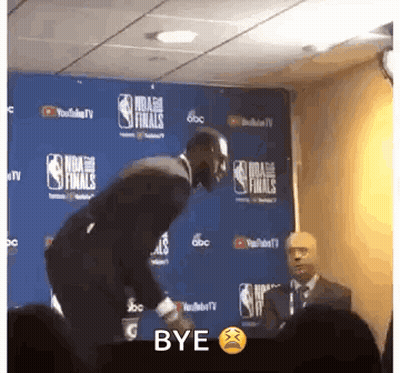 A Man In A Suit Is Standing In Front Of A Wall That Says Nba Finals On It . GIF
