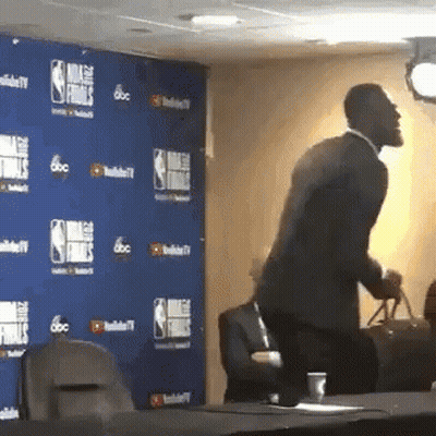 A Man In A Suit Is Standing In Front Of A Wall That Says Nba Finals On It GIF