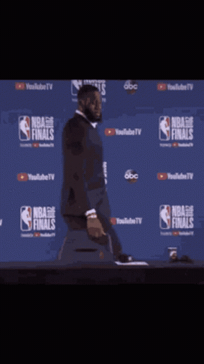A Man In A Suit Is Standing In Front Of A Wall That Says Nba Finals On It GIF