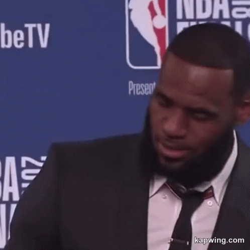 A Man In A Suit Is Standing In Front Of A Wall That Says Nba Finals On It GIF
