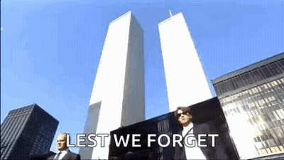 A Man In A Suit Is Standing In Front Of The Twin Towers With The Words Lest We Forget Written Below Him GIF