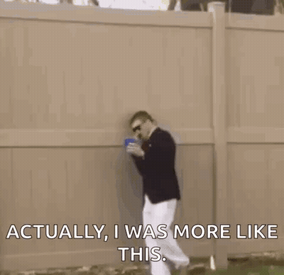 A Man In A Suit Is Standing In The Grass Talking On A Cell Phone While Holding A Cup . GIF