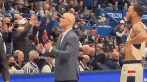 A Man In A Suit Is Standing Next To A Basketball Player In A Stadium . GIF