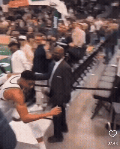A Man In A Suit Is Standing Next To A Basketball Player In The Stands GIF