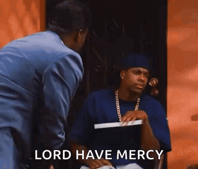 A Man In A Suit Is Standing Next To A Man In A Blue Shirt Who Is Sitting In Front Of A Door . GIF