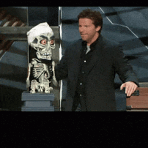 A Man In A Suit Is Standing Next To A Skeleton GIF