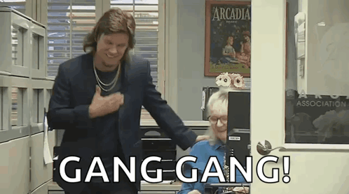 A Man In A Suit Is Standing Next To A Woman In An Office And Says Gang Gang ! GIF