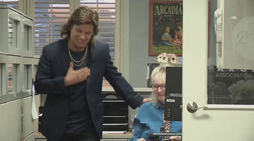 A Man In A Suit Is Standing Next To A Woman In Front Of A Computer With A Poster On The Wall That Says Arcadia GIF
