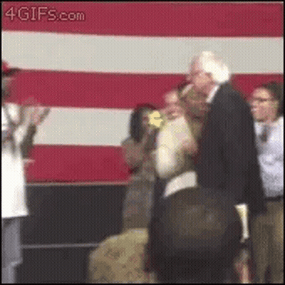 A Man In A Suit Is Standing Next To A Woman In Front Of A Red And White Striped Wall . GIF