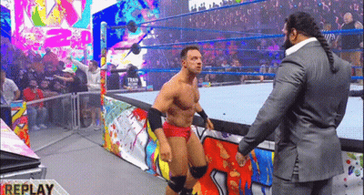 A Man In A Suit Is Standing Next To A Wrestler In A Ring . GIF