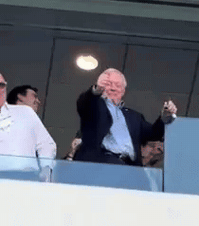 A Man In A Suit Is Standing On A Balcony Pointing At The Camera . GIF