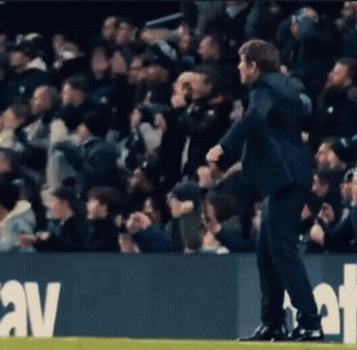 A Man In A Suit Is Standing On A Soccer Field In Front Of A Crowd Of People . GIF