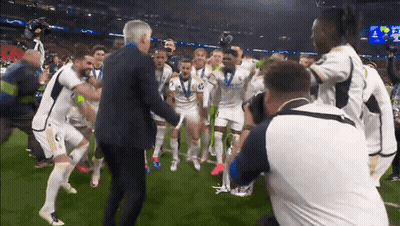 A Man In A Suit Is Surrounded By A Group Of Soccer Players Including One With The Number 2 On His Shirt GIF