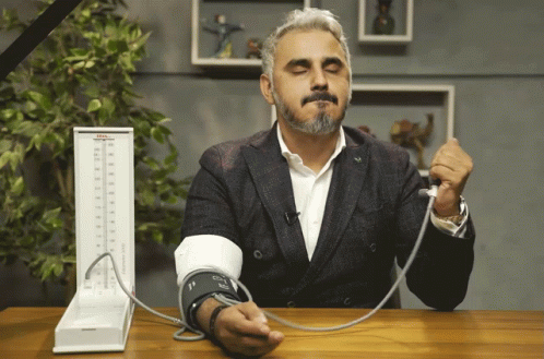 A Man In A Suit Is Taking His Blood Pressure With A Device That Says Tcm GIF