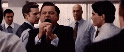 A Man In A Suit Is Talking Into A Microphone While Standing In A Crowd Of People . GIF