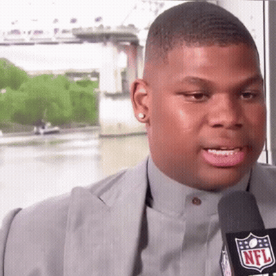 A Man In A Suit Is Talking Into A Microphone With The Nfl Logo On It GIF