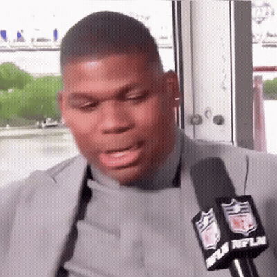 A Man In A Suit Is Talking Into A Microphone With The Nfl Logo On It . GIF