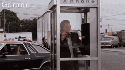 A Man In A Suit Is Talking On A Phone In A Phone Booth GIF