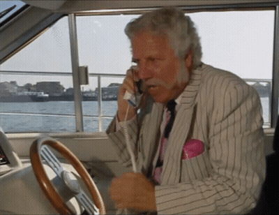 A Man In A Suit Is Talking On A Phone While Driving A Boat GIF