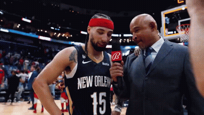 A Man In A Suit Is Talking To A Basketball Player In A New Orleans Jersey GIF