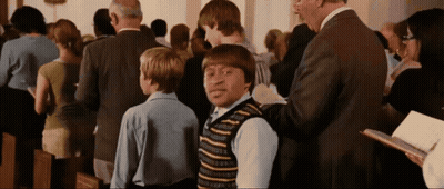 A Man In A Suit Is Talking To A Boy In A Striped Vest In A Church GIF